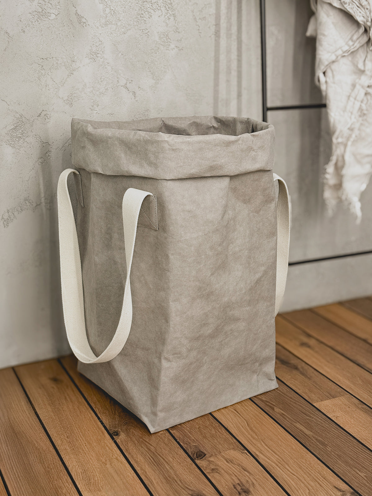 Grey washable paper laundry basket with natural cotton handles beside a ladder rack with a linen throw