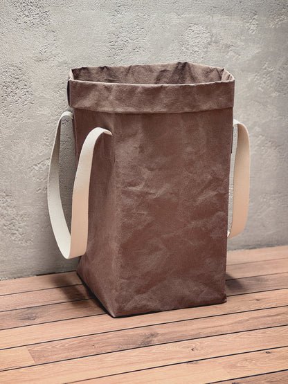 Cocoa washable paper laundry basket with natural cotton handles against a textured wall