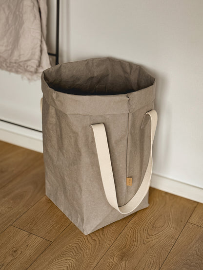 Grey washable paper laundry basket with natural cotton handles on a light wood floor