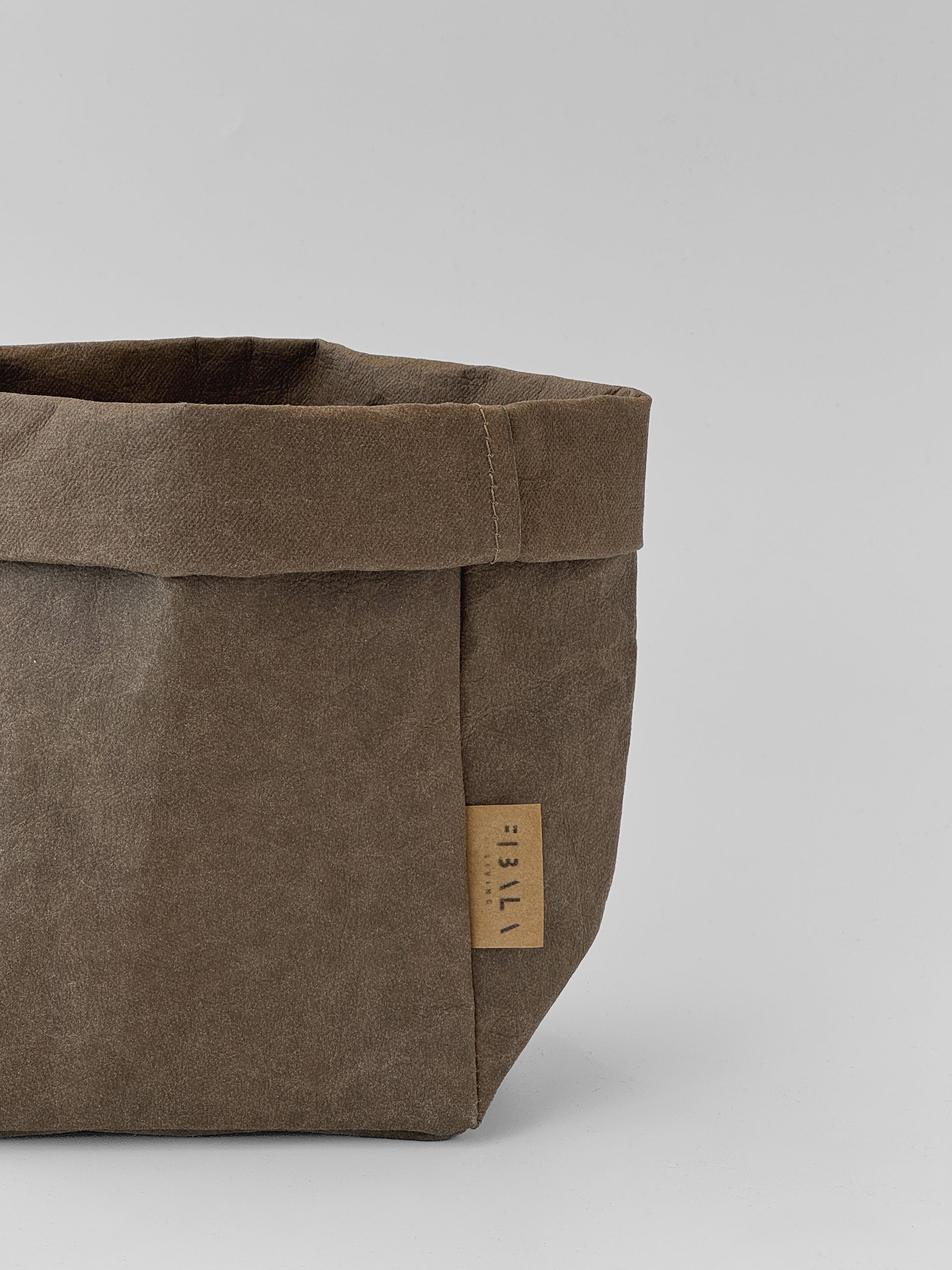 A close-up of a brown washable paper storage basket with a small tan brand tag reading 'Fibala Living' on a light gray background.