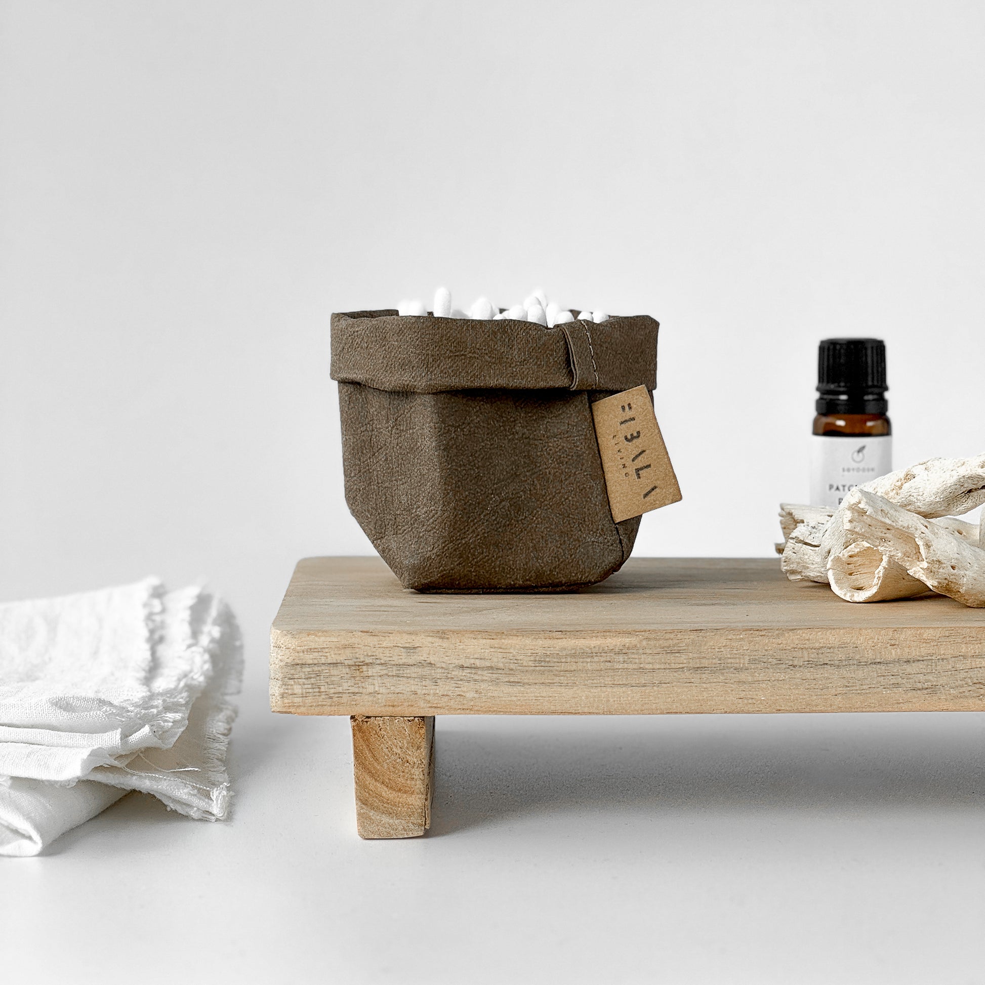 Mini cocoa brown washable paper bag, tag on wood stand, white fabric & bottle—natural spa style setup 