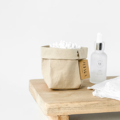 Mini sand beige washable paper bag, white earbuds, wood surface—eco chic mini tote