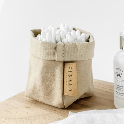 Side-view mini sand beige washable paper bag, white earbuds, wood surface—eco chic mini tote