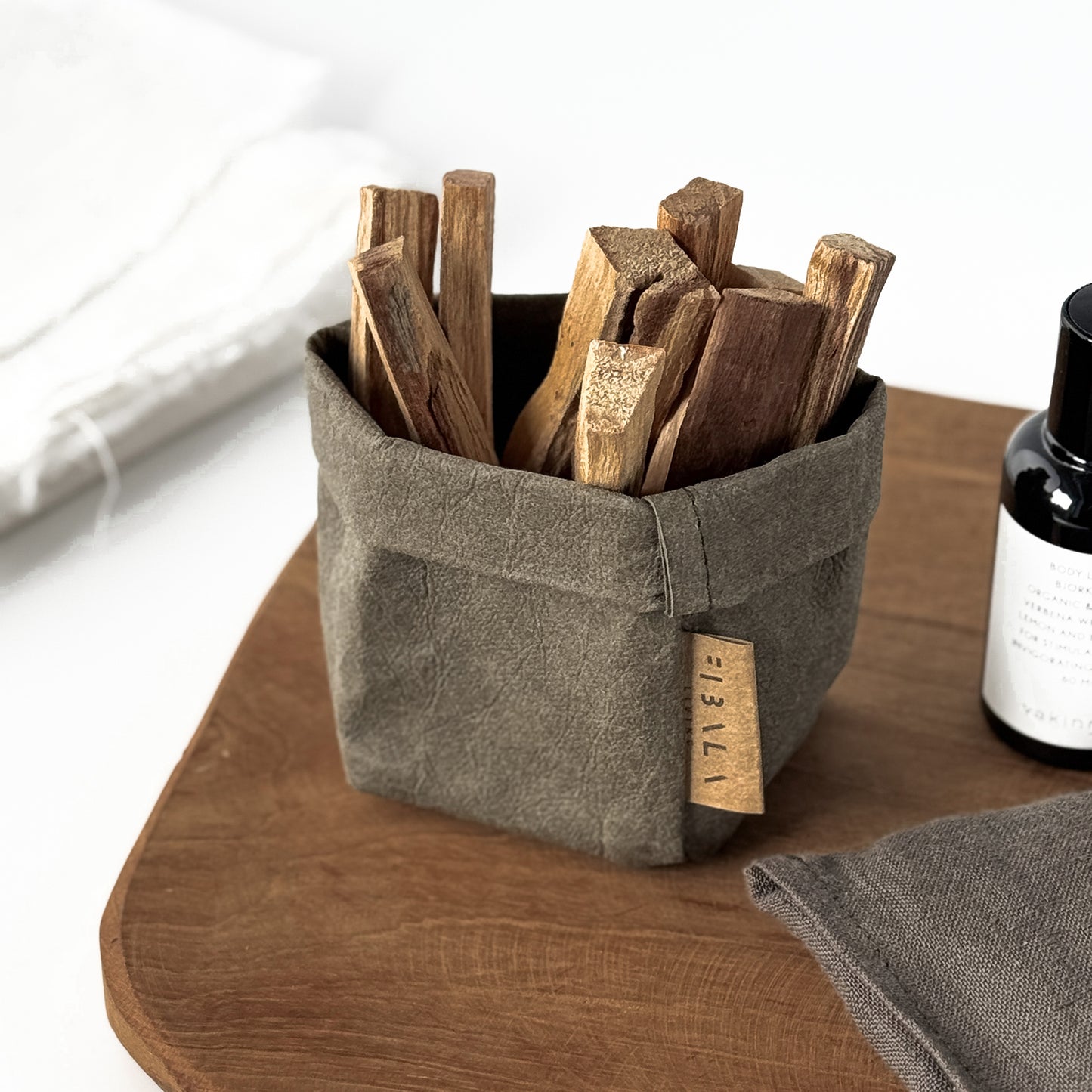 Top-view XS olive-green washable paper bag, wooden sandal sticks, bottle, towel, wood surface—eco mini tote