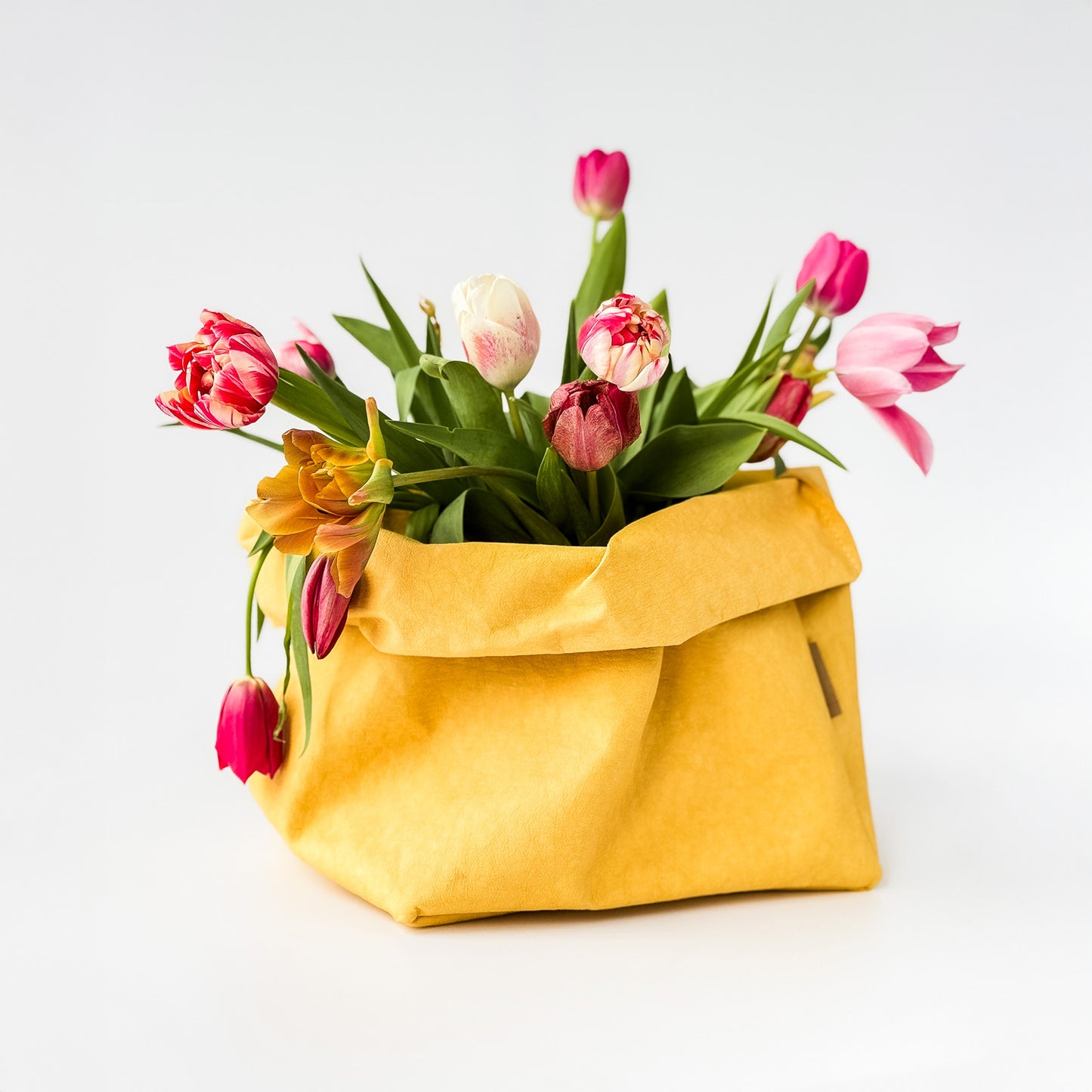 Yellow washable paper bag filled with colorful tulips on a white background
