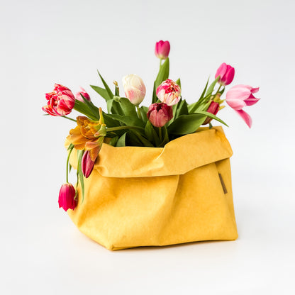 Yellow washable paper bag filled with colorful tulips on a white background
