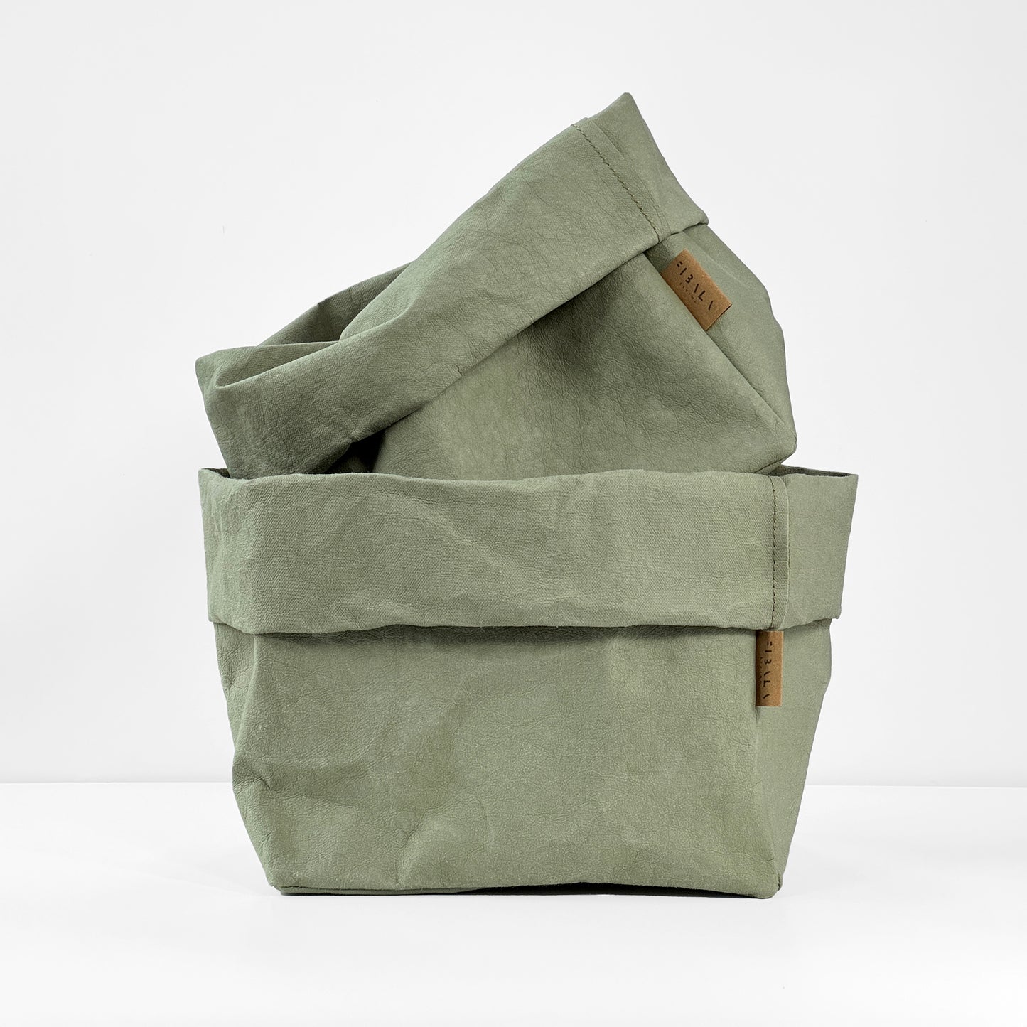 Sage washable paper bags stacked toghether with a brand label on a white background