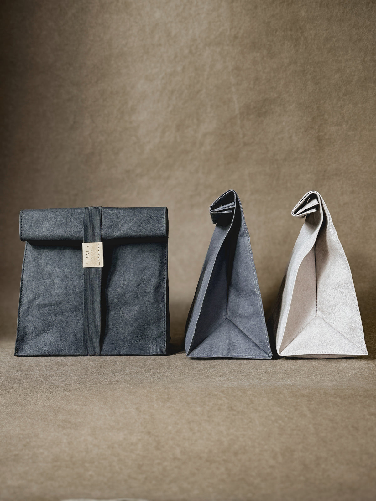 Three washable paper lunch bags in black, steel and light grey with roll-top closures