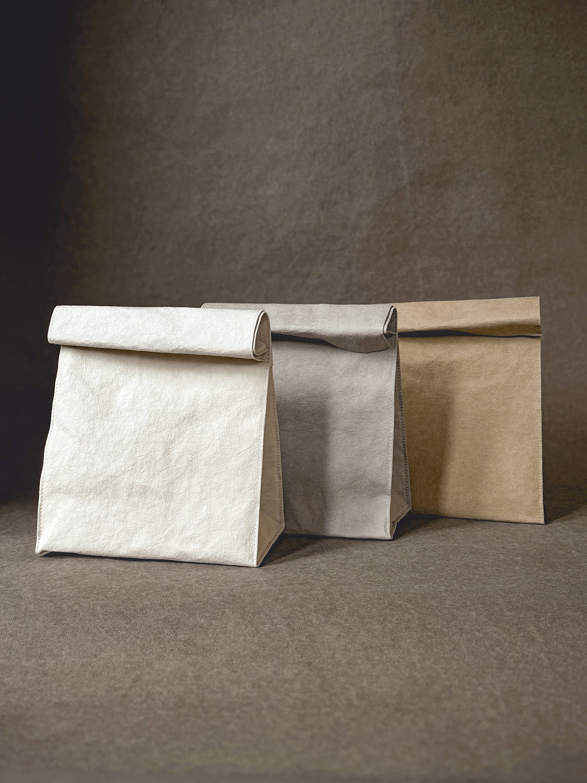 Three washable paper lunch bags in light neutral colors standing side by side
