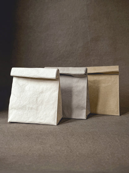 Three washable paper lunch bags in light neutral colors standing side by side