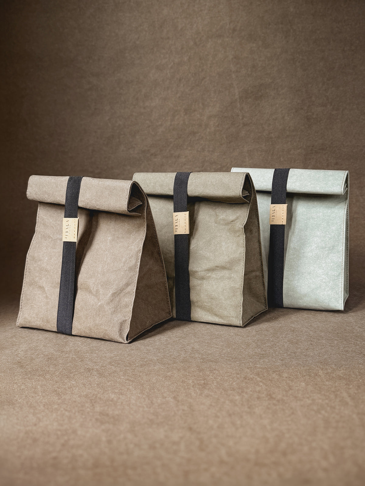 Three washable paper lunch bags in neutral colors, each closed with a black elastic band
