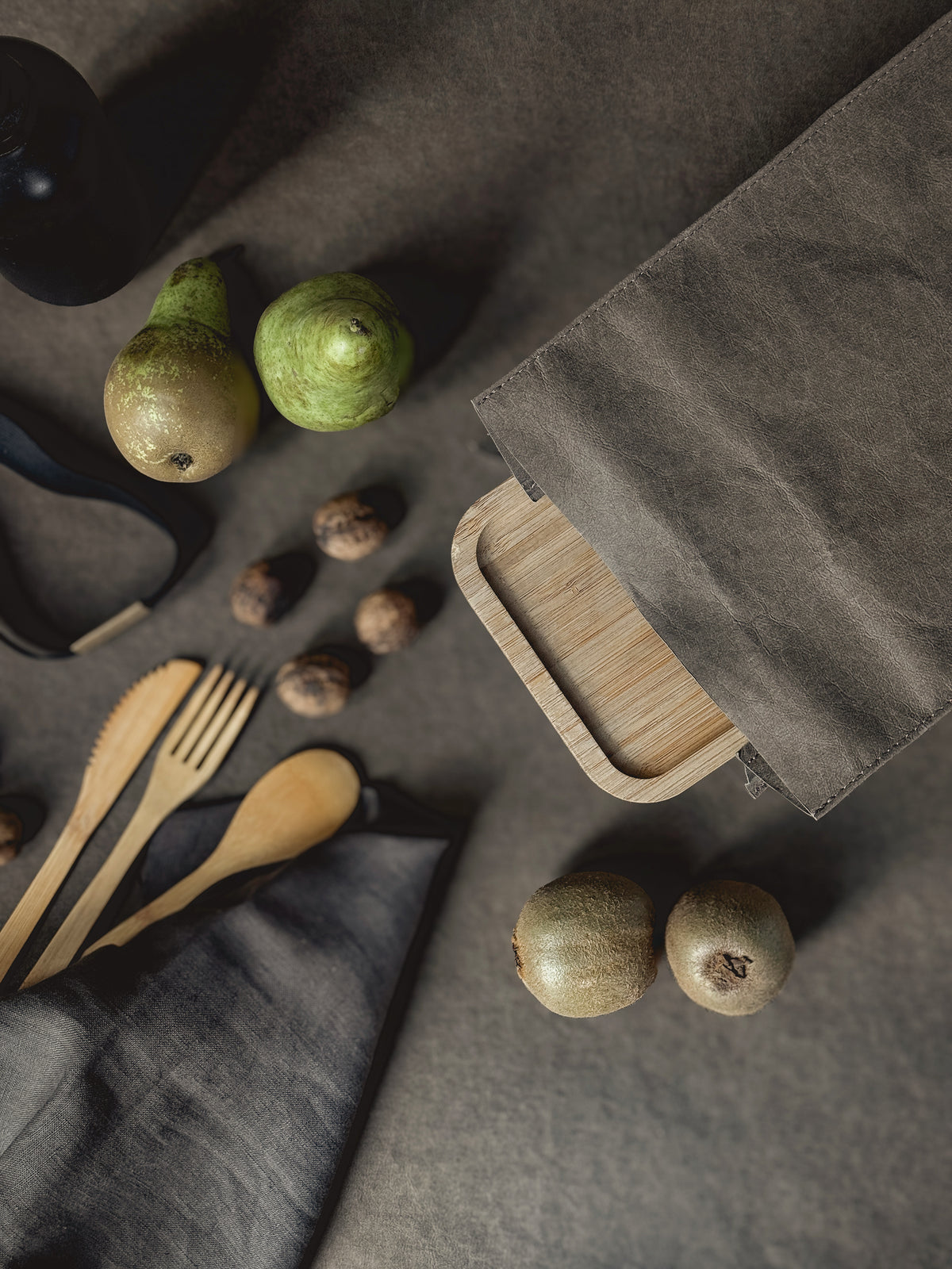 Bamboo lunch box sliding into a washable paper lunch bag, with pears, walnuts and wooden cutlery