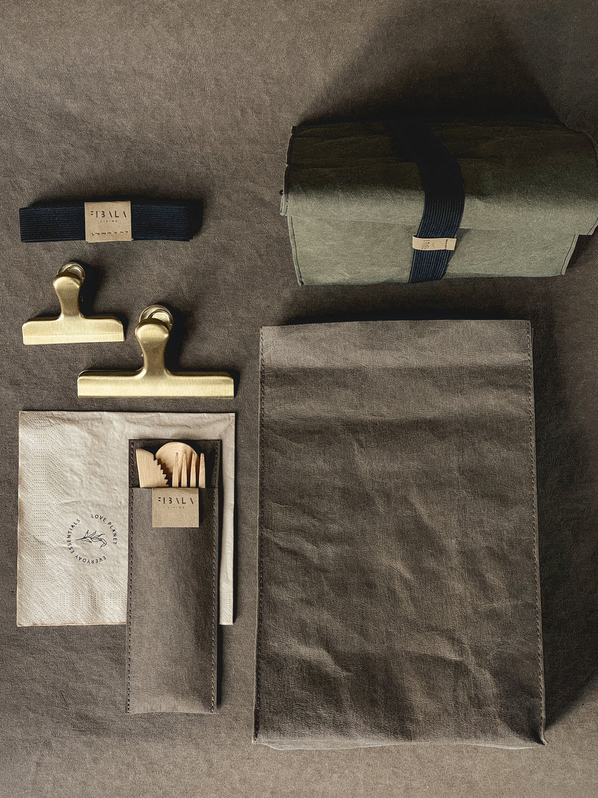 Washable paper lunch bag laid flat with the matching cutlery pouch, bamboo cutlery, napkin and elastic band
