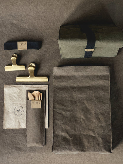 Washable paper lunch bag laid flat with the matching cutlery pouch, bamboo cutlery, napkin and elastic band