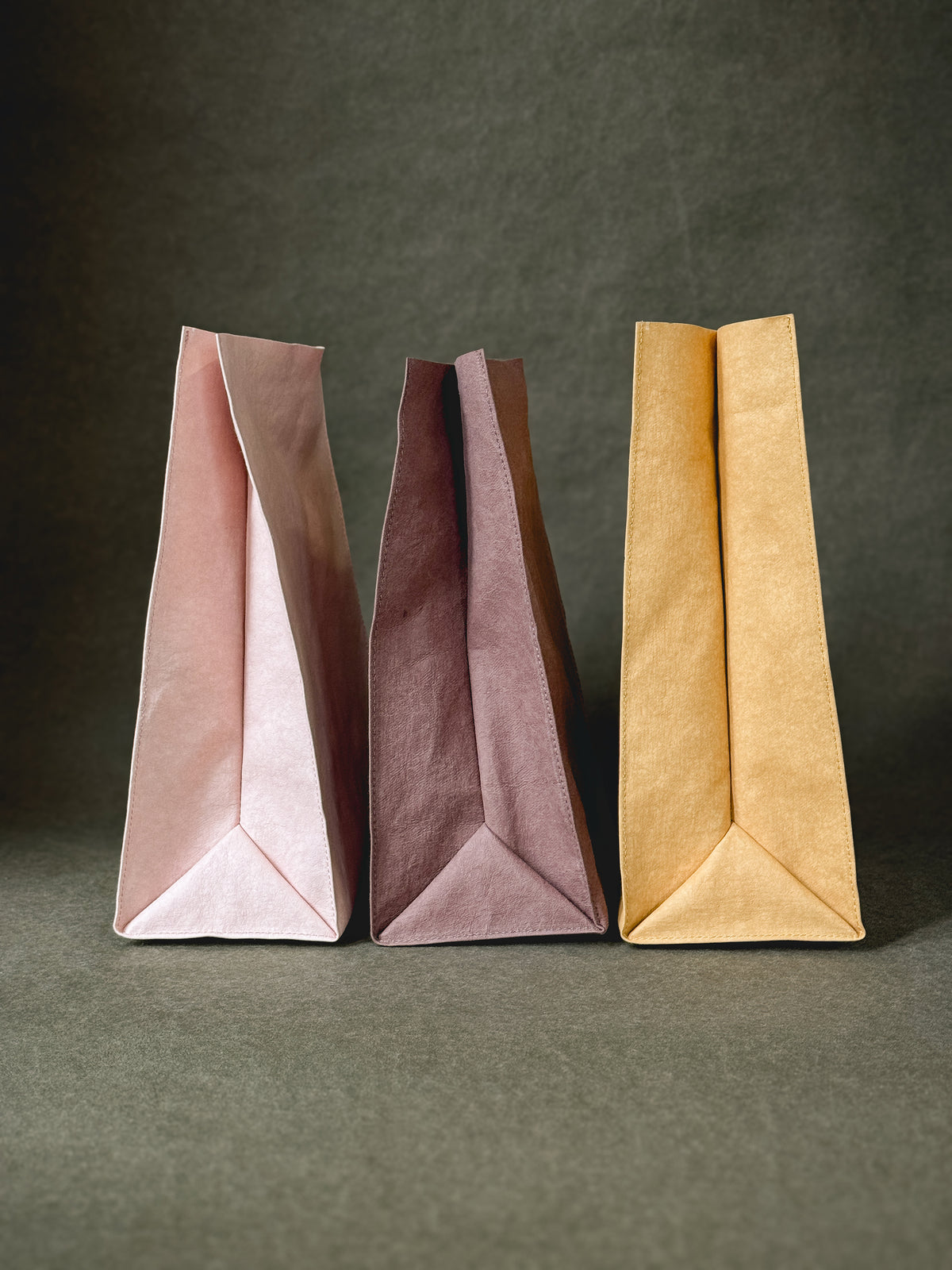 Three washable paper lunch bags in rose, fig and mustard, shown from the side with the folded base