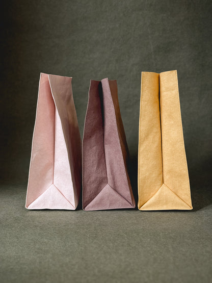 Three washable paper lunch bags in rose, fig and mustard, shown from the side with the folded base