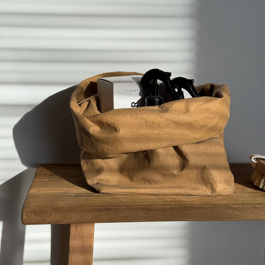 Large brown washable paper bag on wooden surface, against white wall. Handmade, sustainable, perfect for simple living.