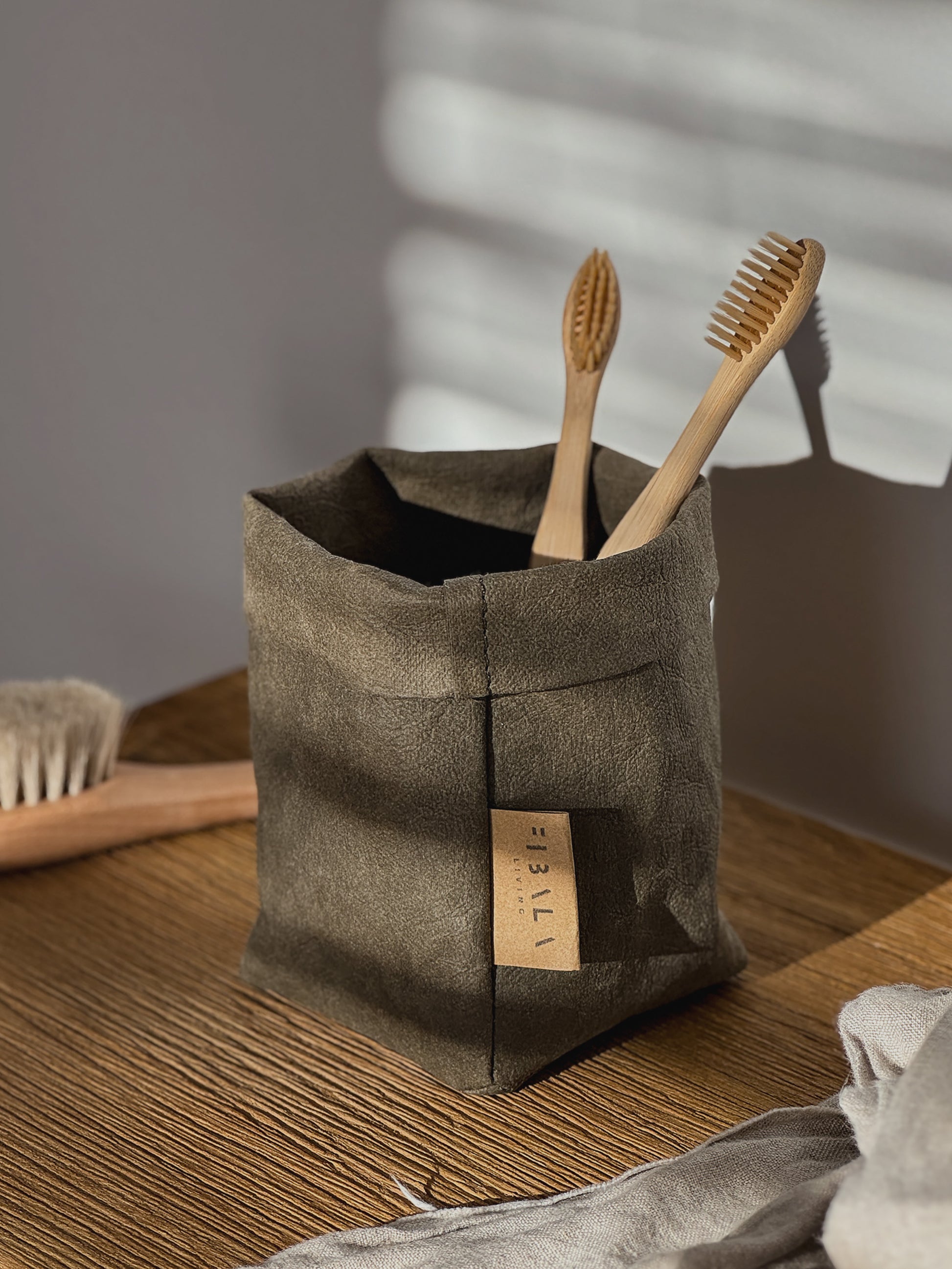 Olive washable paper bag with wooden toothbrushes on a wooden surface.