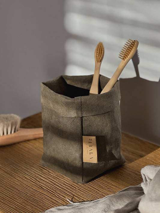 Olive washable paper bag with wooden toothbrushes on a wooden surface.