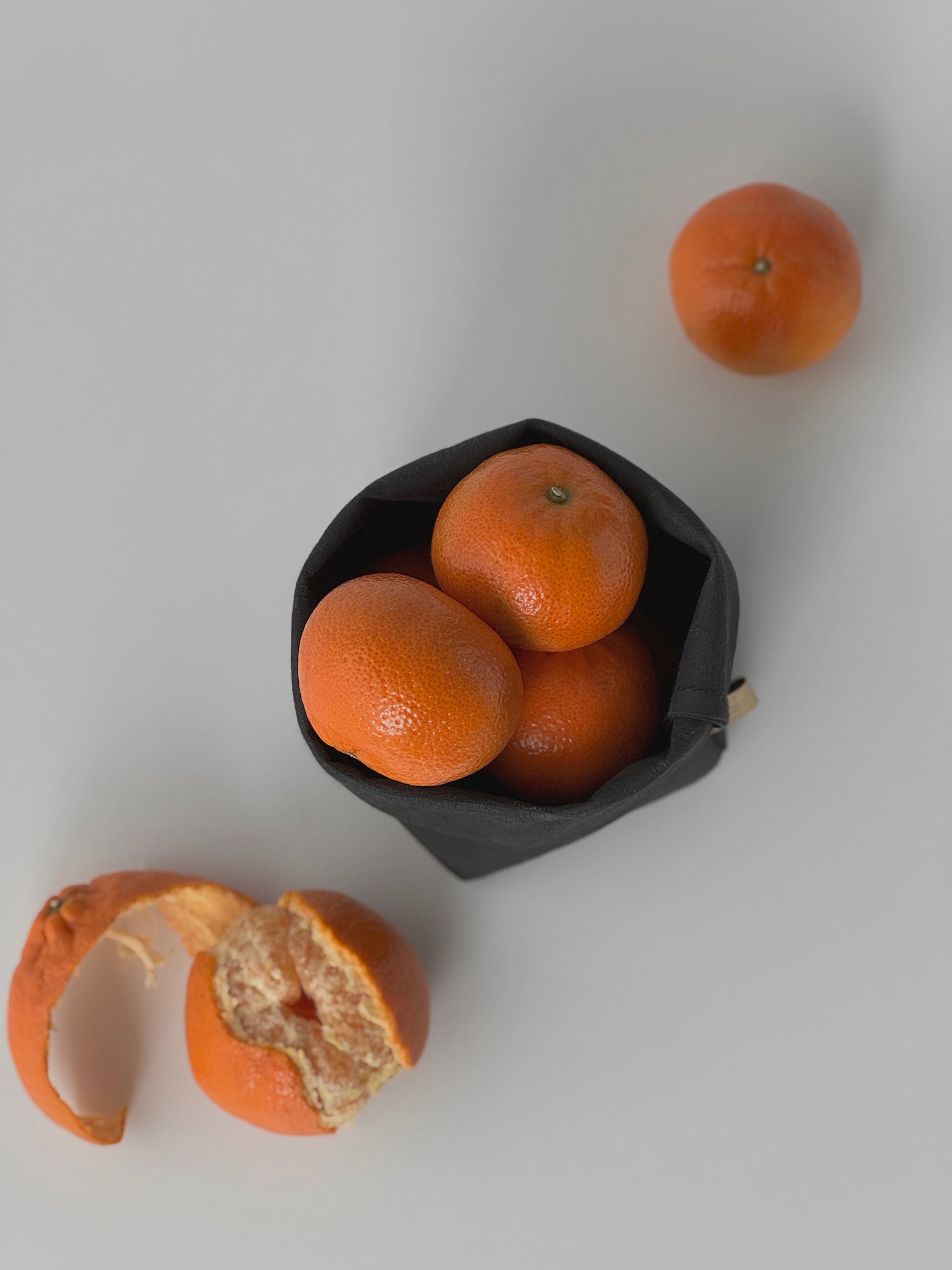 Mandarines in washable paper storage bag with a peeled one on a light gray background