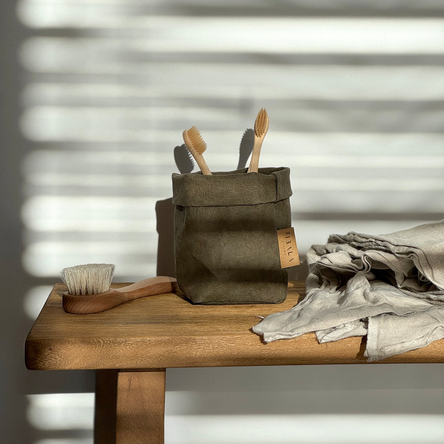 Petite olive green washable paper bag, wooden brushes, wood table, front view—eco mini tote