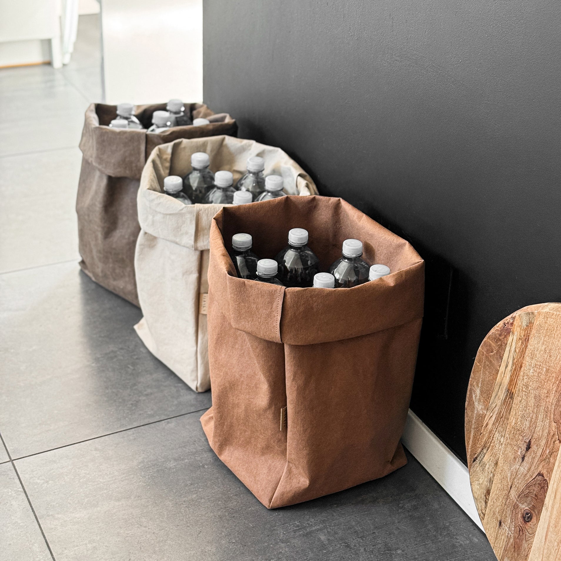 XXL washable paper bags store water bottles on kitchen tile, black wall—sustainable recycling storage