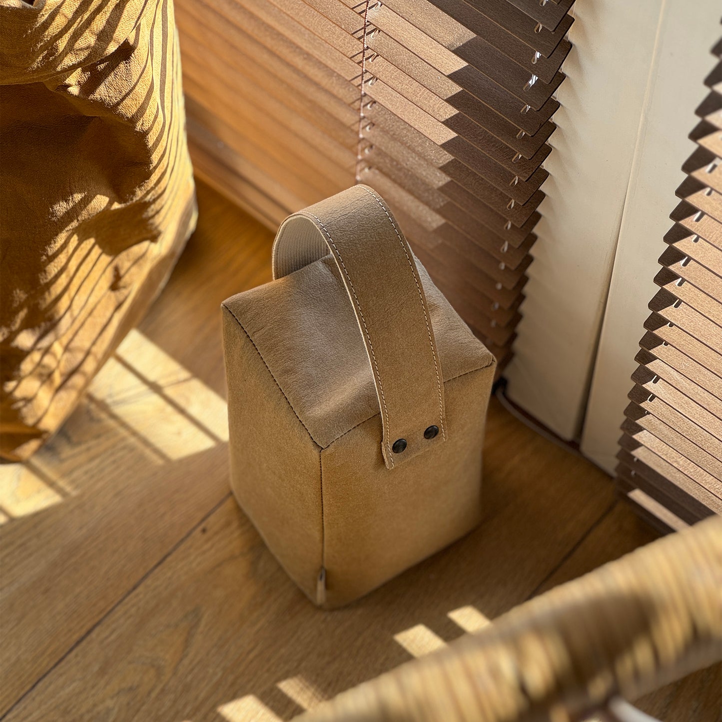 Brown cube washable paper doorstop on wood floor, matching bag behind, eco-safe wedge