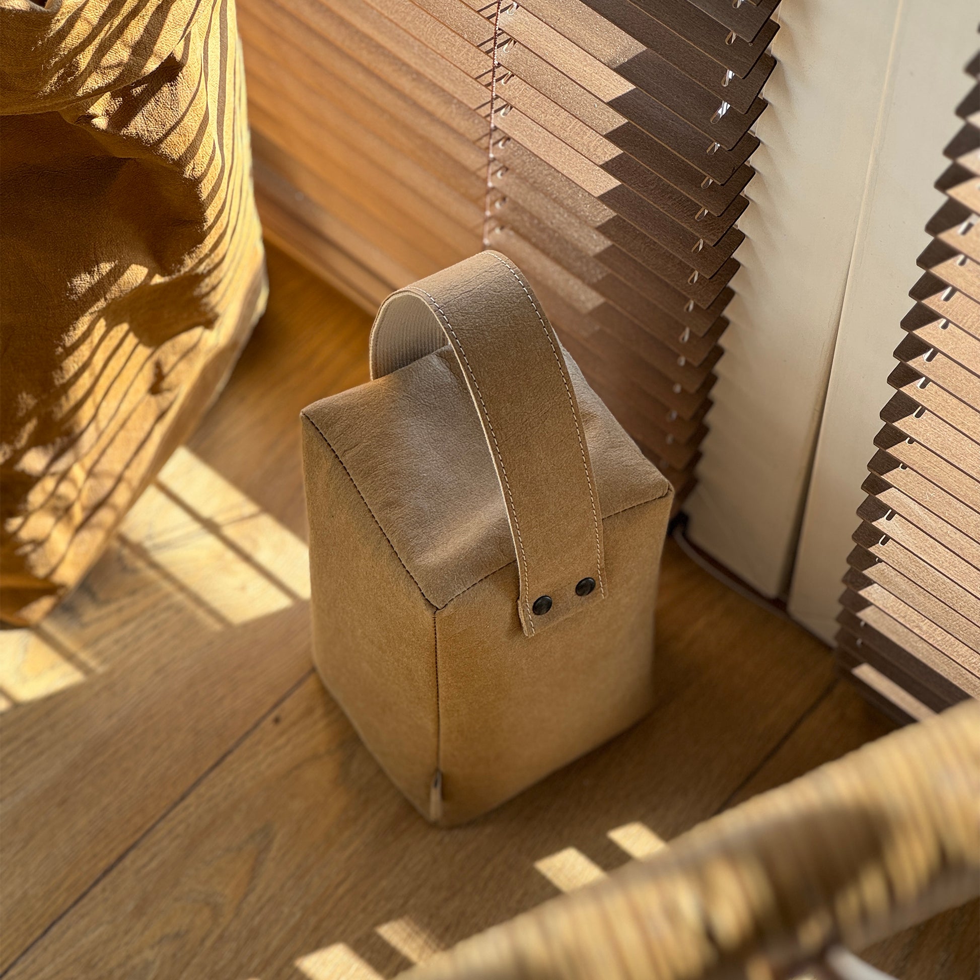 Brown cube washable paper doorstop on wood floor, matching bag behind, eco-safe wedge