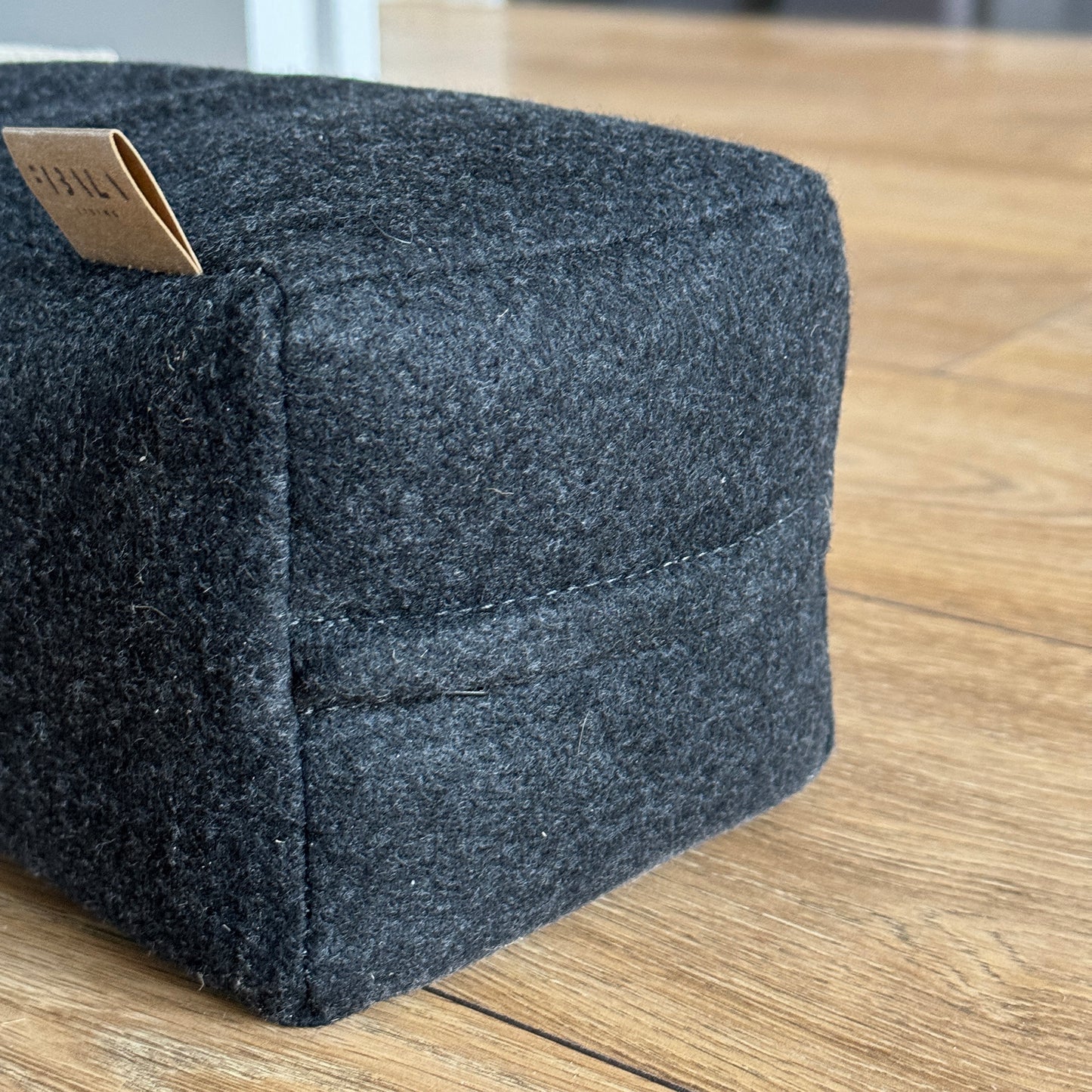 Close-up dark gray wool zip doorstop, angled sides, soft felt texture, tiny tag, minimalist eco wedge