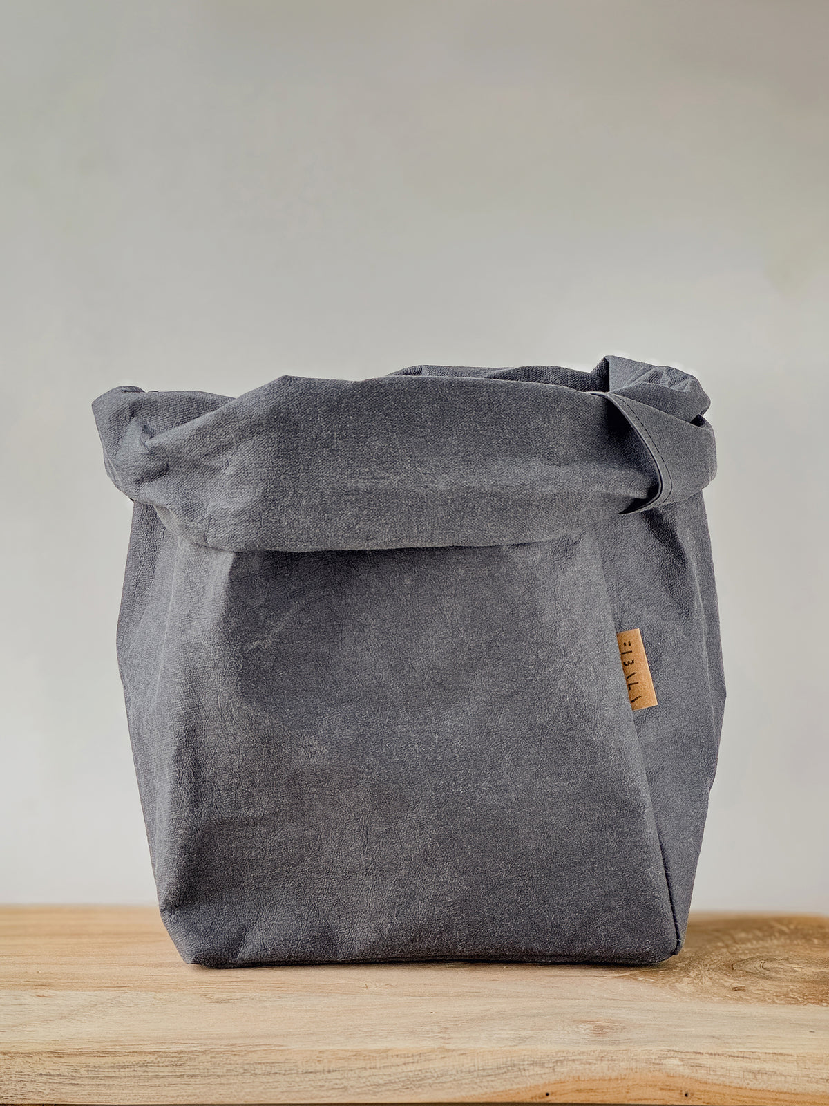 Dark grey XL washable paper storage bag with a rolled top on a wooden bench