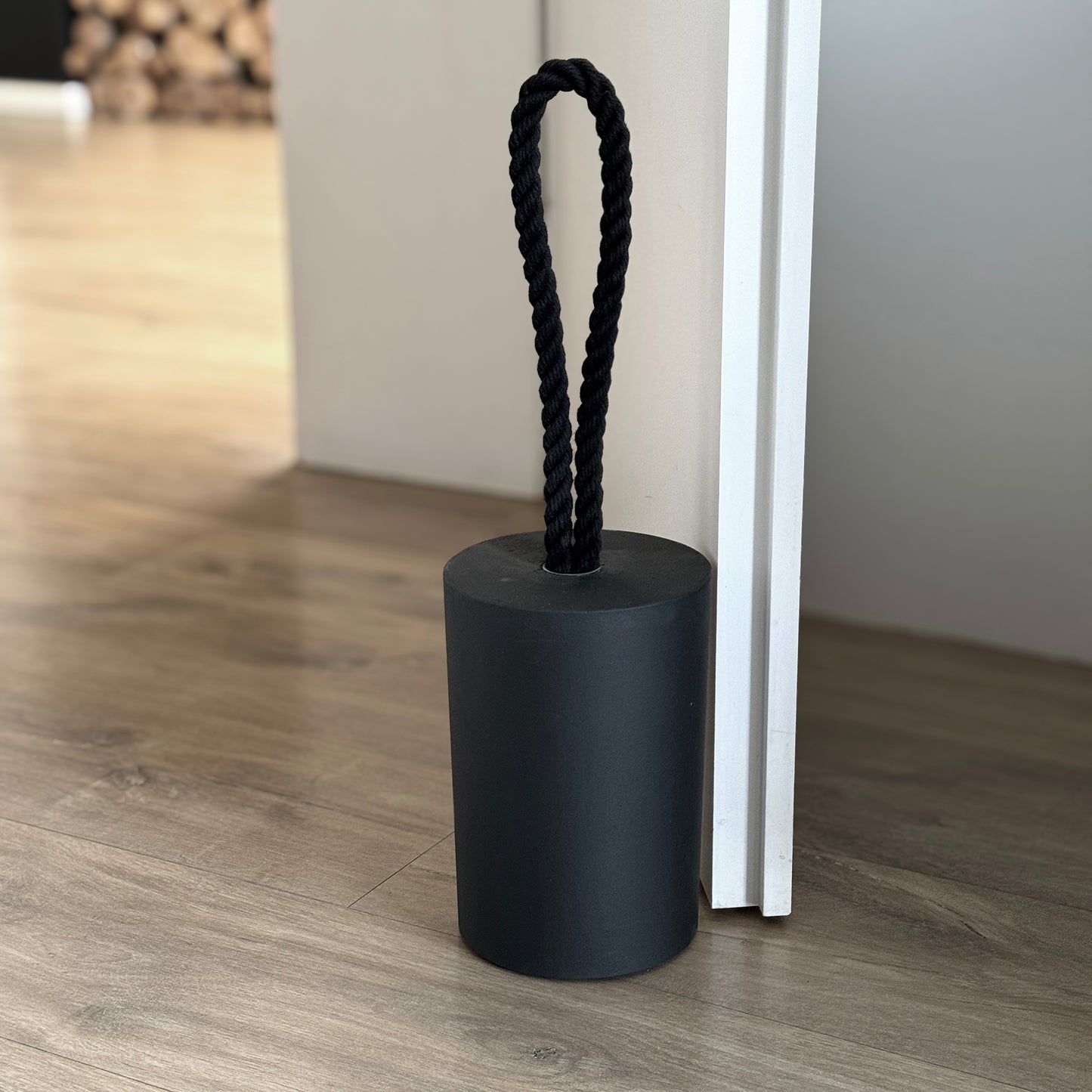 Close-up, top-down view of an extra large black concrete door stop with a loop-style black cotton rope handle. The image highlights the raw, textured concrete surface and the twisted rope detail, showcasing its sturdy build and minimalist design. A functional, stylish piece for modern interiors and exteriors.