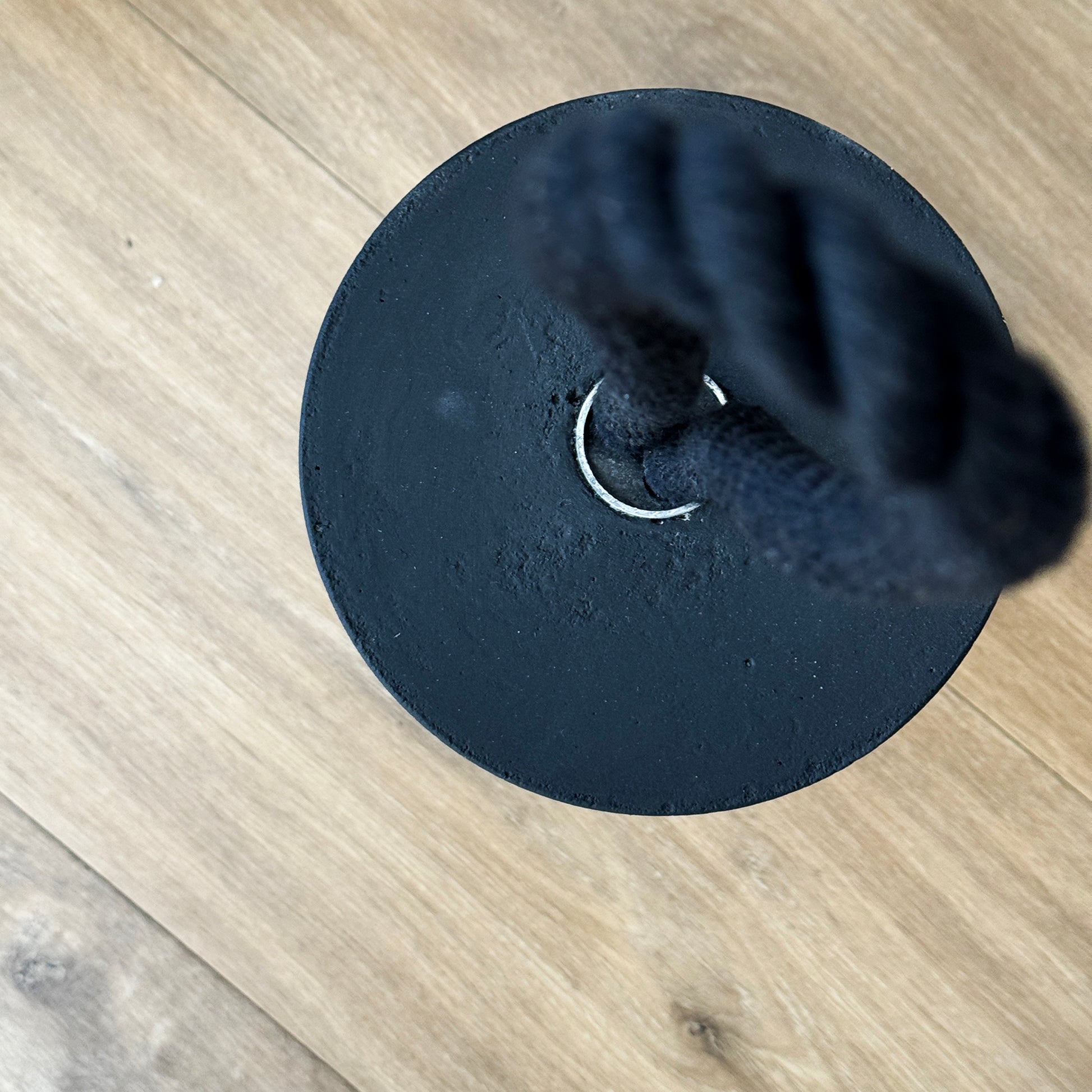 Top-down view of an extra large black concrete door stop, showcasing its smooth cylindrical shape and solid concrete base. The black cotton rope handle appears slightly blurred in the background, keeping focus on the raw texture and clean lines of the concrete. A sleek, functional accent for modern minimalist interiors and exteriors.