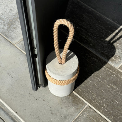 top view of minimalist gray concrete door stop with jute handle and rustic wrap, placed near a patio door on stone flooring — heavy modern doorstop for indoor and outdoor use