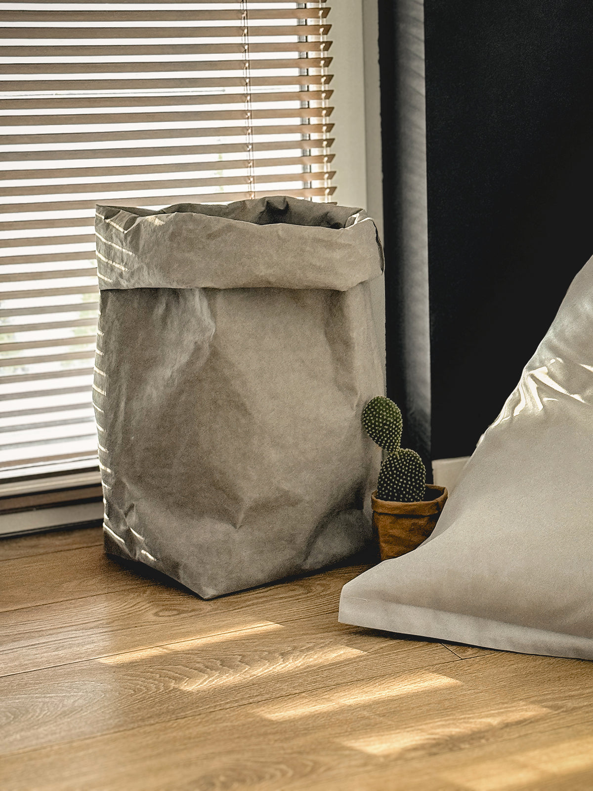 XXL washable paper storage bag by a window next to a small cactus and a floor cushion
