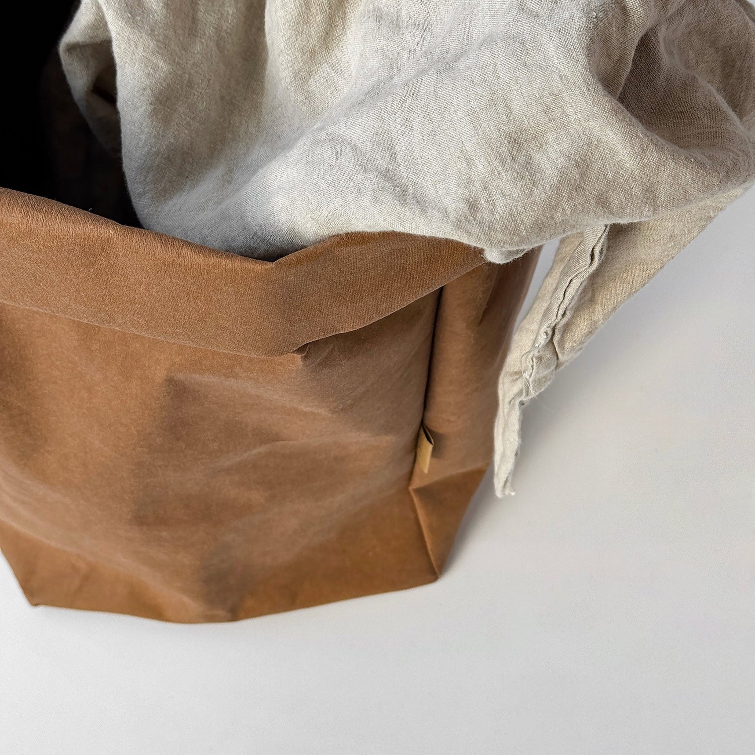 Top-view XXL brown washable paper bag, beige linen throw inside, white BG, eco storage