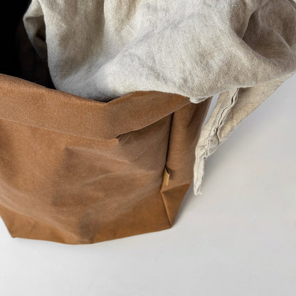 Top view of XXL brown washable paper bag with beige linen throw inside, on white background | Eco-friendly, versatile storage solution