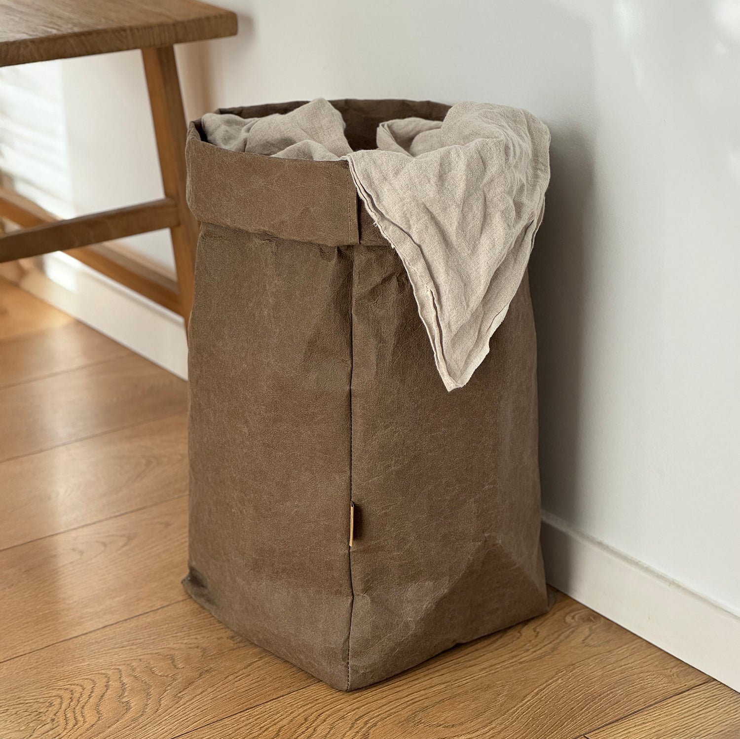 Side-view XXL cocoa washable paper bag, linen throw fill, wood floor, white wall, eco storage
